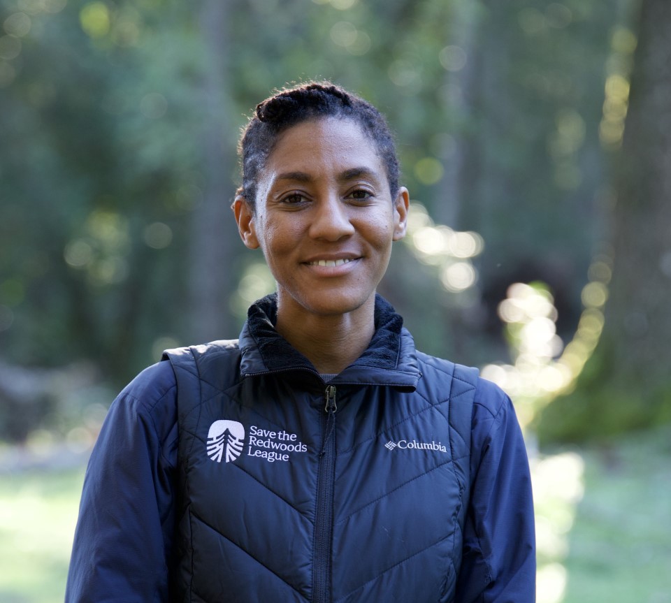 a woman wearing a Save the Redwoods vest smiles at the camera