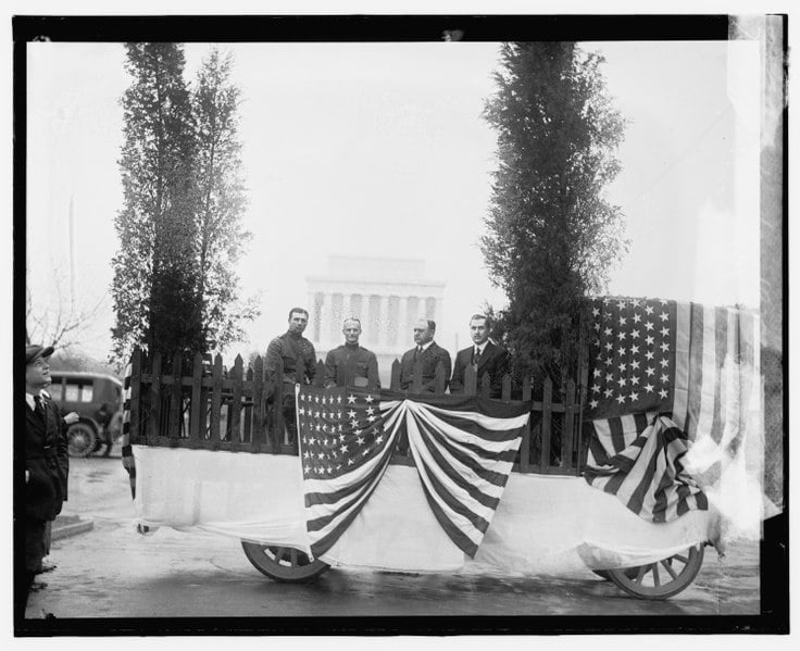 Four people ride in a float with young trees and American flags