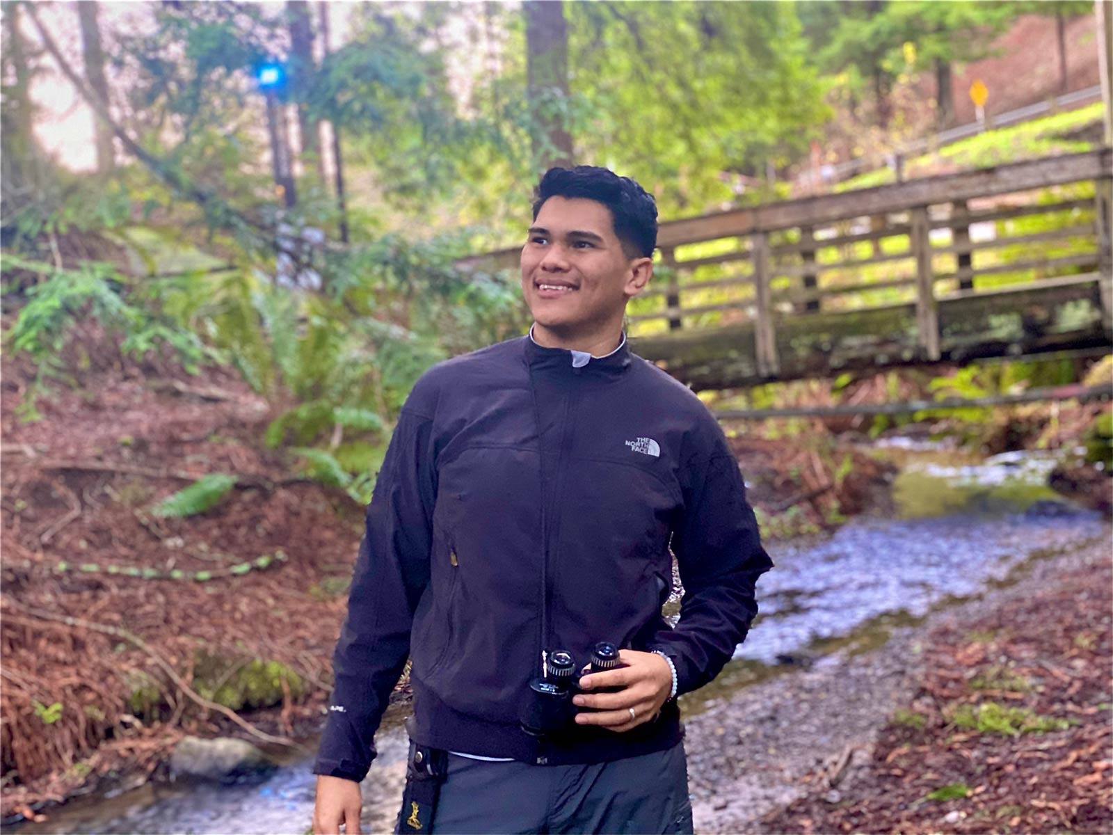 BIPOC starter grant field researcher holding binoculars by a creek outside