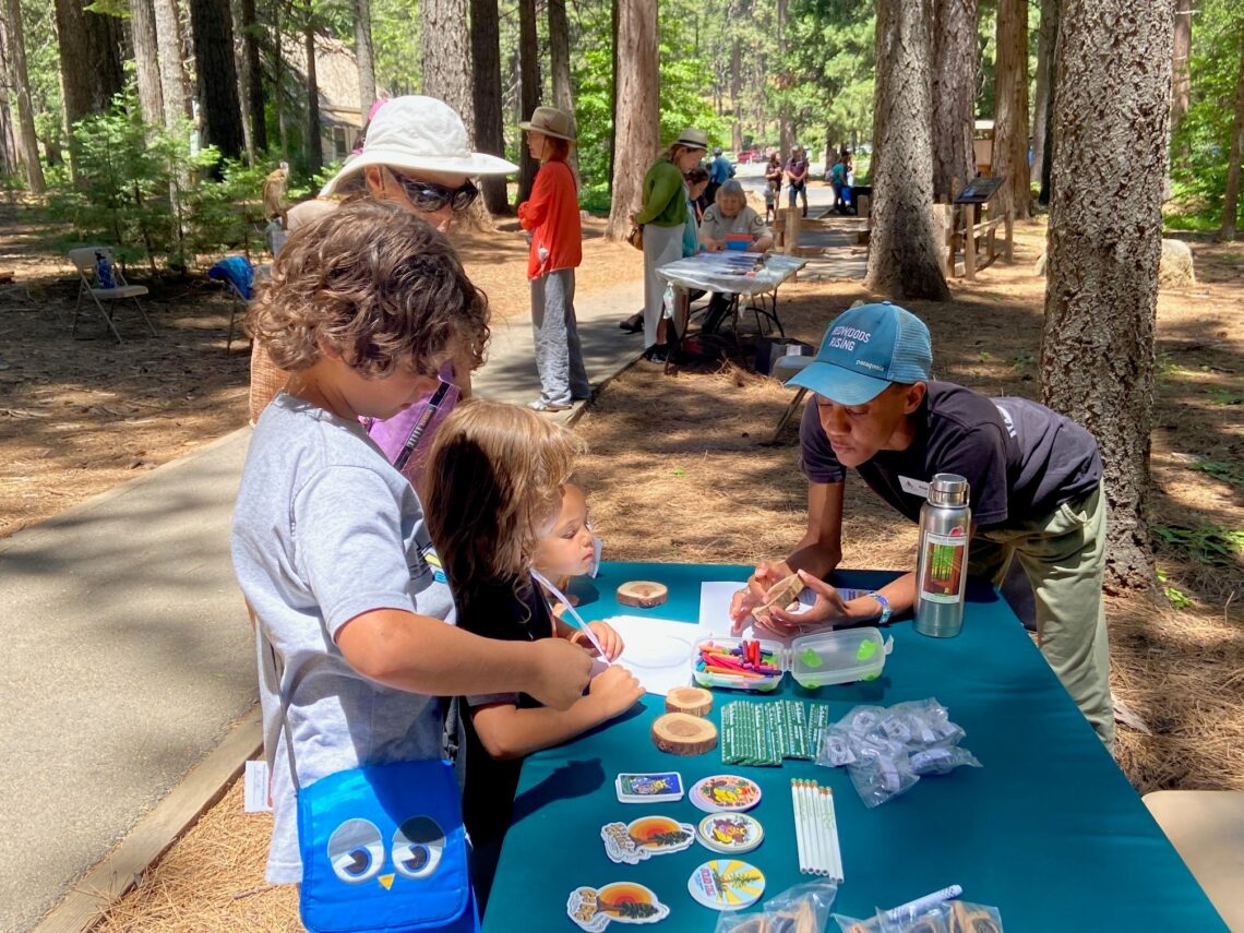 A woman explains a cross section of redwood to children at an outdoor booth