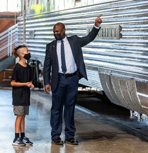 A picture containing an adult and child wearing masks next to a train