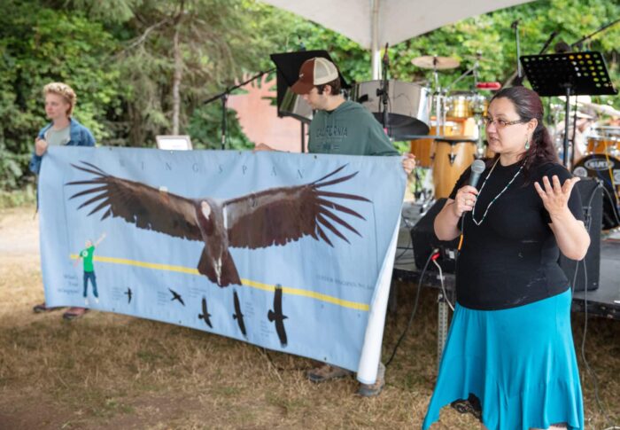A woman with a microphone talks next to a banner showing a California condor.