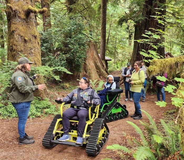 People ride in an electric all-terrain chair through Prairie Creek Redwoods.