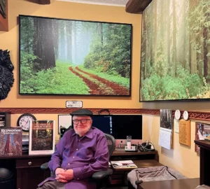 Portrait of a person at a desk in a room beneath large landscape photographs of redwoods