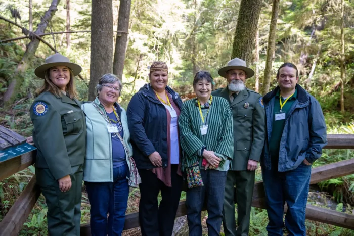 A group of seven people, some wearing rangers uniforms, pose for a photo in the redwoods