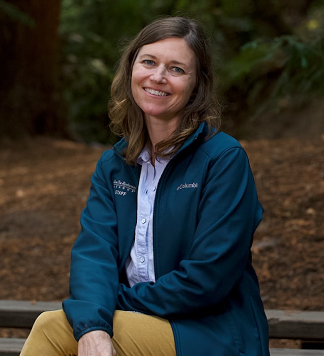 A woman wearing a dark teal jacket, sitting in a coast redwood forest