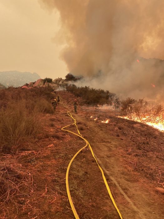 Firefighters on a ridge with a handline along a ridge with fire and smoke