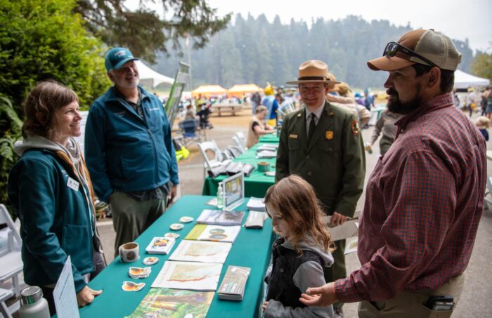 Two staff members with Save the Redwoods League talk with visitors at a display table