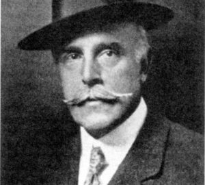 Historical photo of an older man in a suit, with a mustache and fedora hat