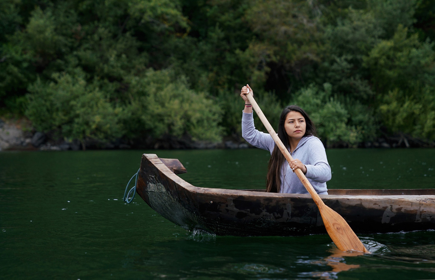 Young woman paddling a redwood canoe on the river