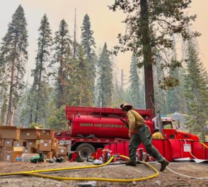 Fire fighter walks in front of water tanker during forest fire.