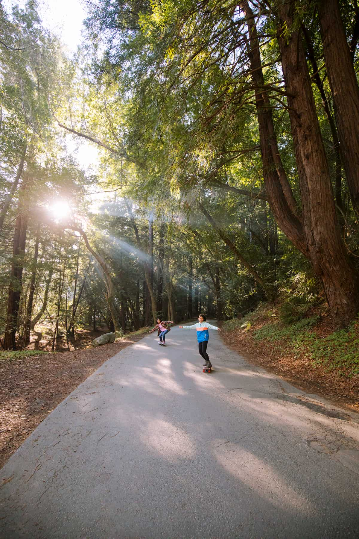 Two women ride down a paved road on longboards with knees bent and arms outstretched as they carve into their turns.