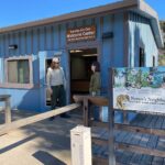 A ranger standing in front of the new Rancho del Oso Welcome Center - a blue and brown building with interpretive signage in front.