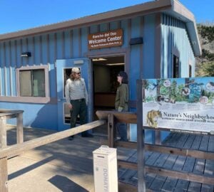 A ranger standing in front of the new Rancho del Oso Welcome Center - a blue and brown building with interpretive signage in front.