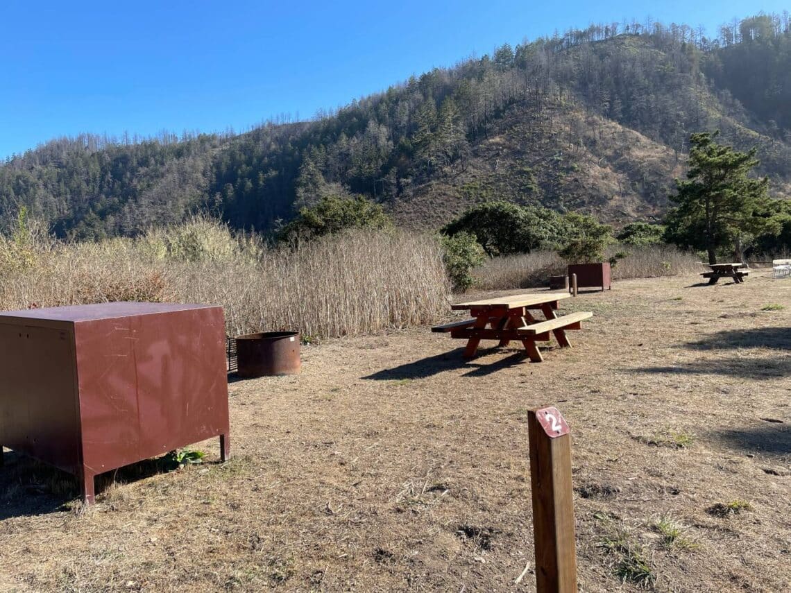 A campground with bear locker, tables and fire pit.