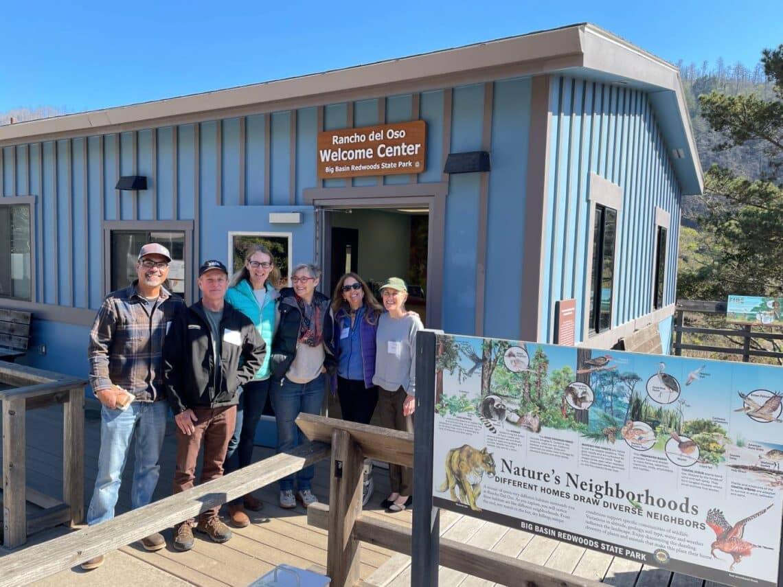 Six people smile at the doorway to a welcome center.