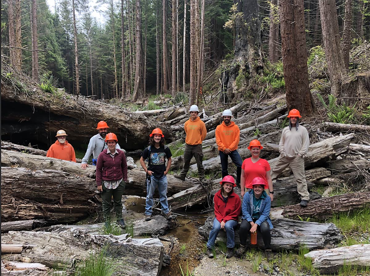 10 apprentices from 2022 Apprenticeship program standing outdoors in a forest with hardhats on