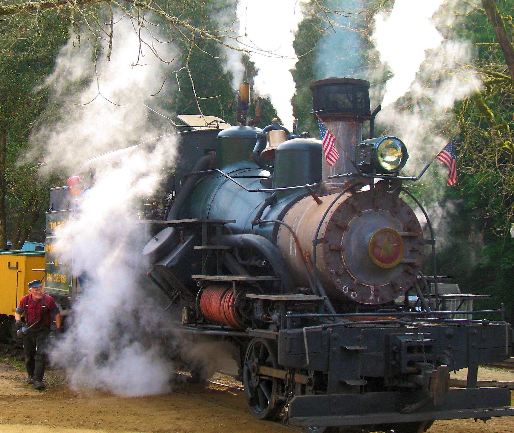 Dramatic clouds of steam escape from a black steam locomotive as an oilman walks alongside with an oil can