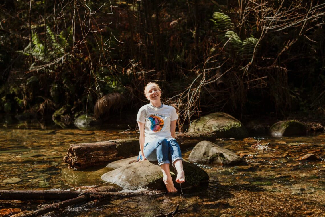 A woman sits on a rock in the middle of a creek