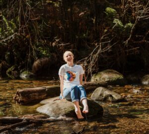 A woman sits on a rock in the middle of a creek