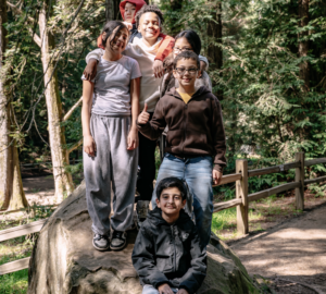 a group of kids, standing or sitting around a large rock, pose for the camera