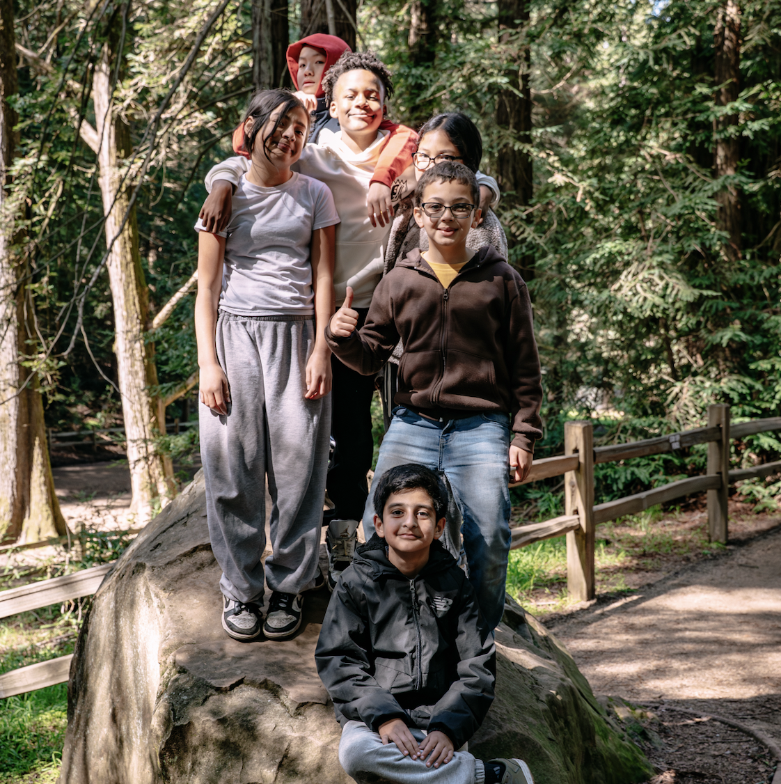 a group of kids, standing or sitting around a large rock, pose for the camera