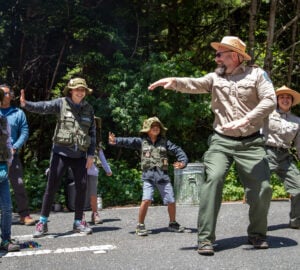 A man in a state parks uniform leads a group of young people in a dance
