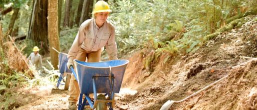 Trail crew member pushes wheelbarrow.