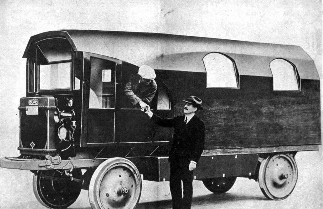 An antiqued black and white photograph of Charles Kellogg leaning out the window from the drivers seat of his his Travel Log, the world's first recreational vehicle, made from a fallen redwood log. By Robert H. Moulton, American Forestry 24 (297): 528-530., Public Domain, Wiki Commons: https://commons.wikimedia.org/w/index.php?curid=77254508.