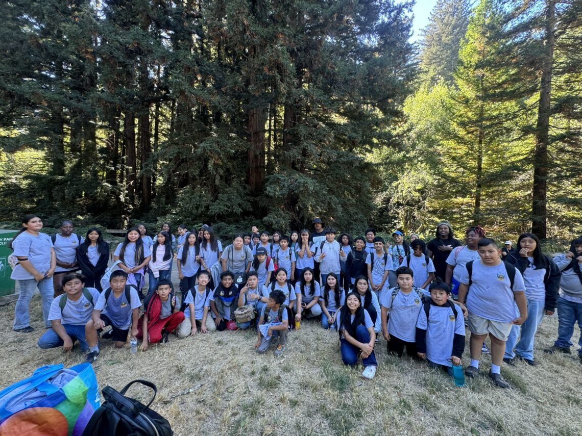 a large group of students wearing light blue uniform shirts poses for a group photo