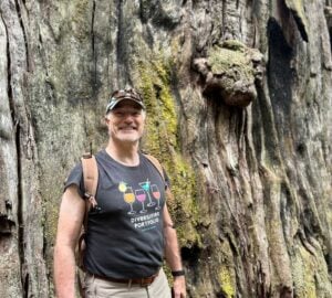 Daen Wombwell standing in front of an ancient redwood tree.
