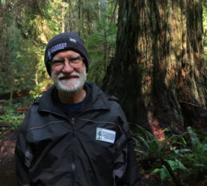 A smiling person shown from chest up in a redwood forest.