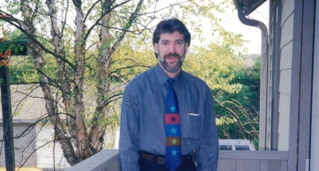 Dr. Craig White, a white man with dark hair and salt and pepper beard, wearing a blue shirt and a tie. 