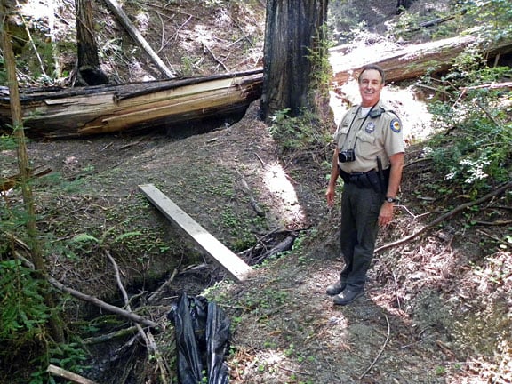 Ranger Wiegman stands at a section of trail in need of an 18 foot bridge replacement. A wooden plank acts as a temporary bridge for Park staff to access this area, which is still closed to the public.