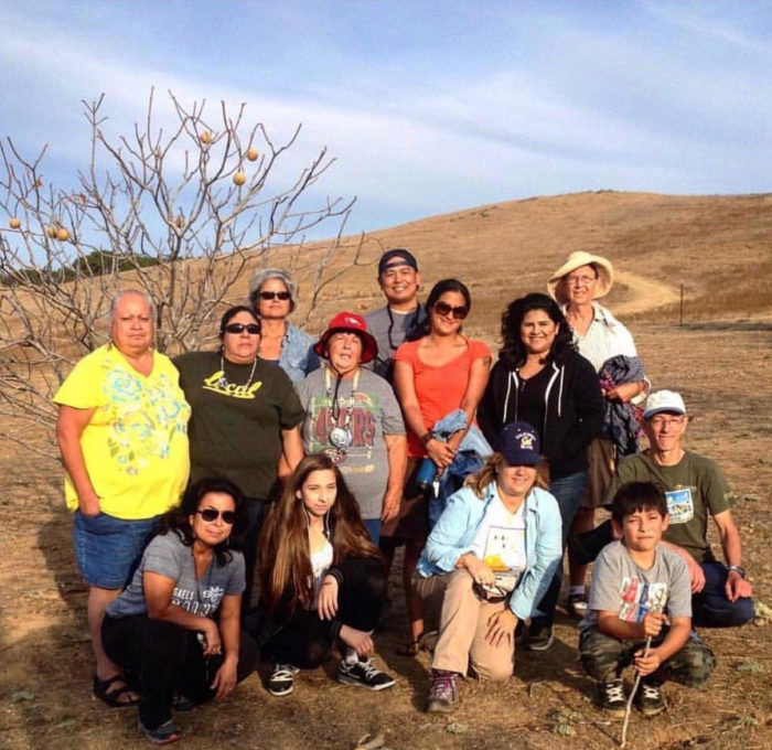 A group of people stand in front of a buckeye tree on a golden hill