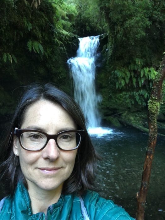 A brunette woman wearing glasses in front of a waterfall