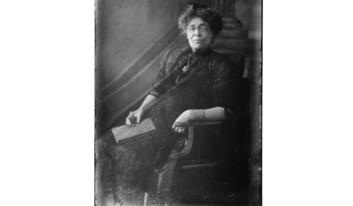 Oldl black-and-white photo of a woman sitting in a chair and holding a book.