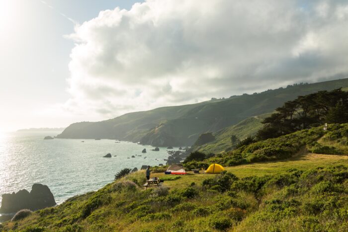 Two tents sit on a green plateau overlooking the Pacific Ocean.