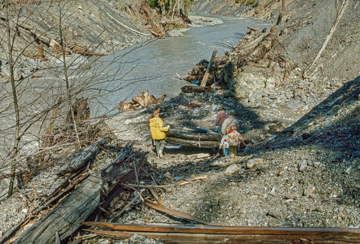 People walking a raft through a rocky creek bed toward a river filled with murky water.