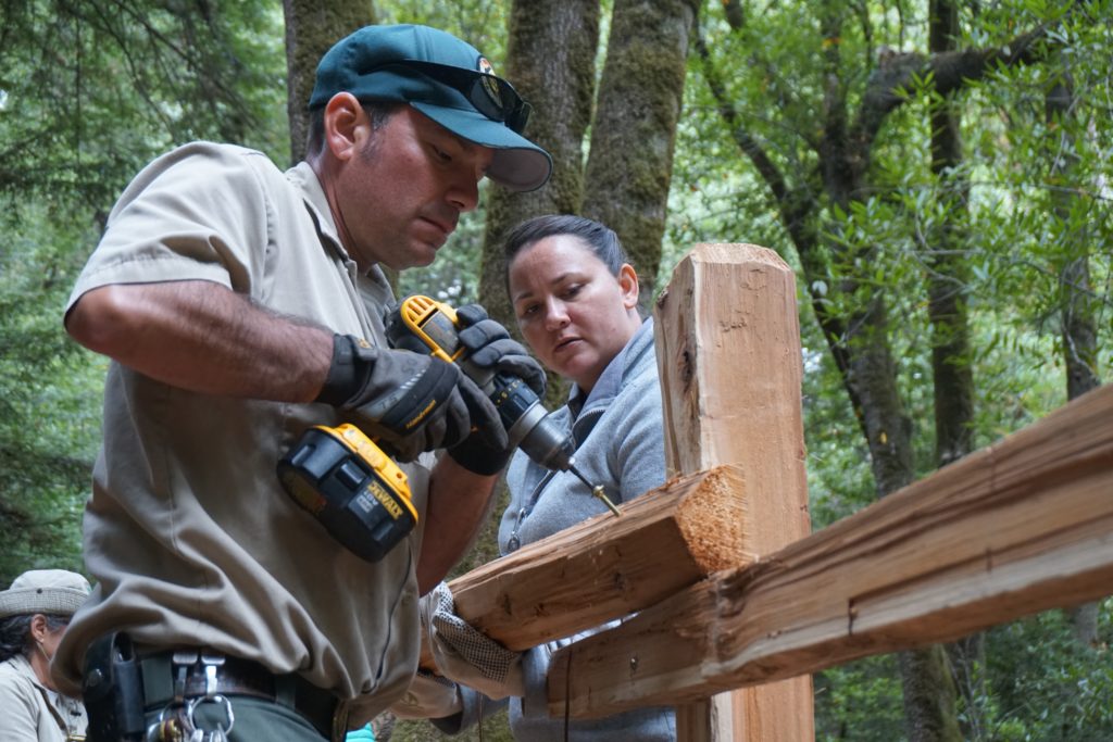 A volunteer holds up a fence beam for the park ranger to secure.