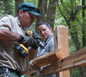 A volunteer holds up a fence beam for the park ranger to secure.